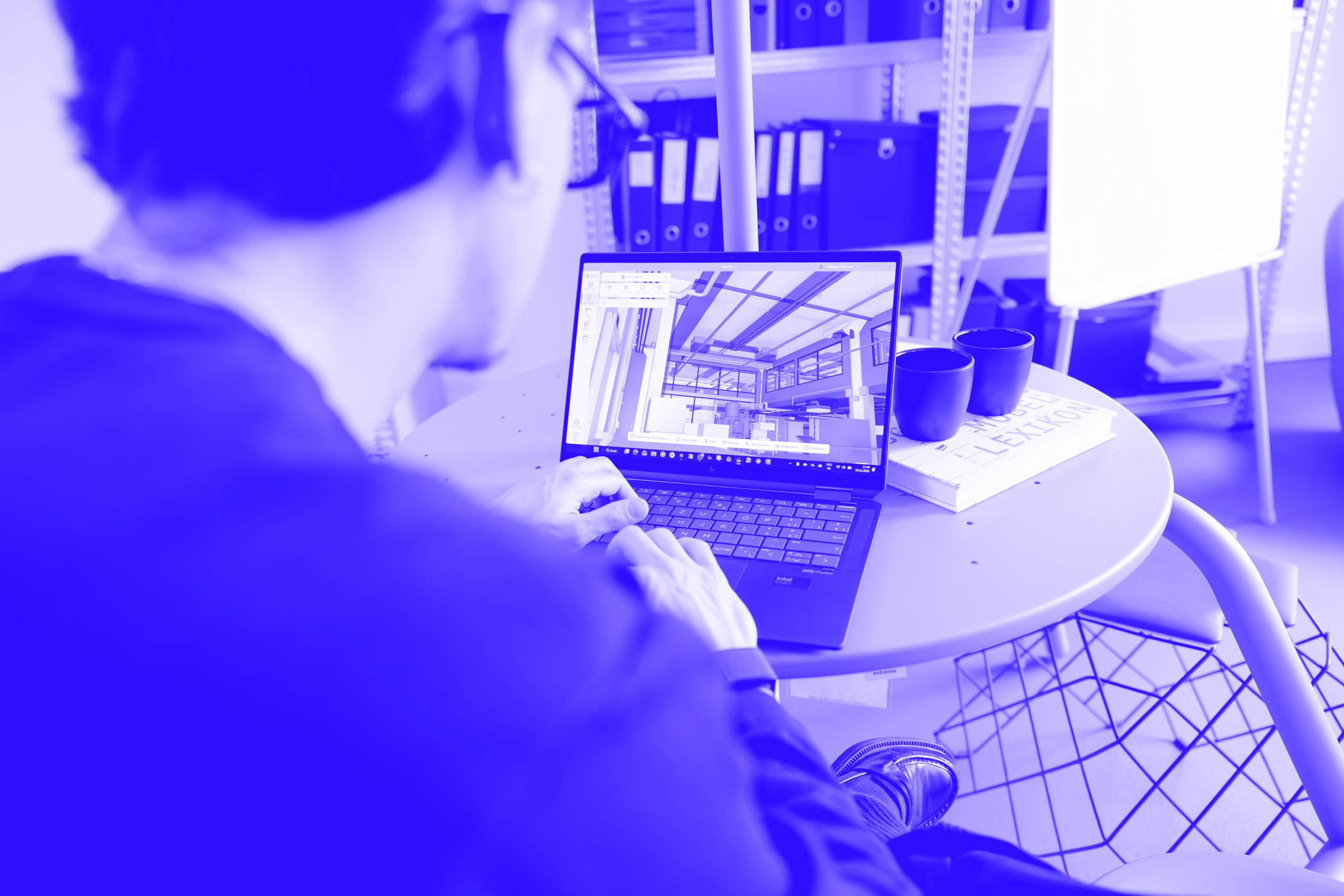 Fabiano mit aufgeklappten Laptop und digitalem Modell offen, dass Bild ist mit dem Impuls+ blau eingefärbt