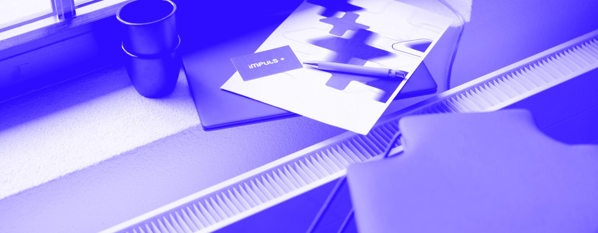 Detailshot von Laptop, Visitenkarte Impuls+ und Blatt mit Logo von Impuls Plus GmbH. Digitalisierung für mehr Zeit.